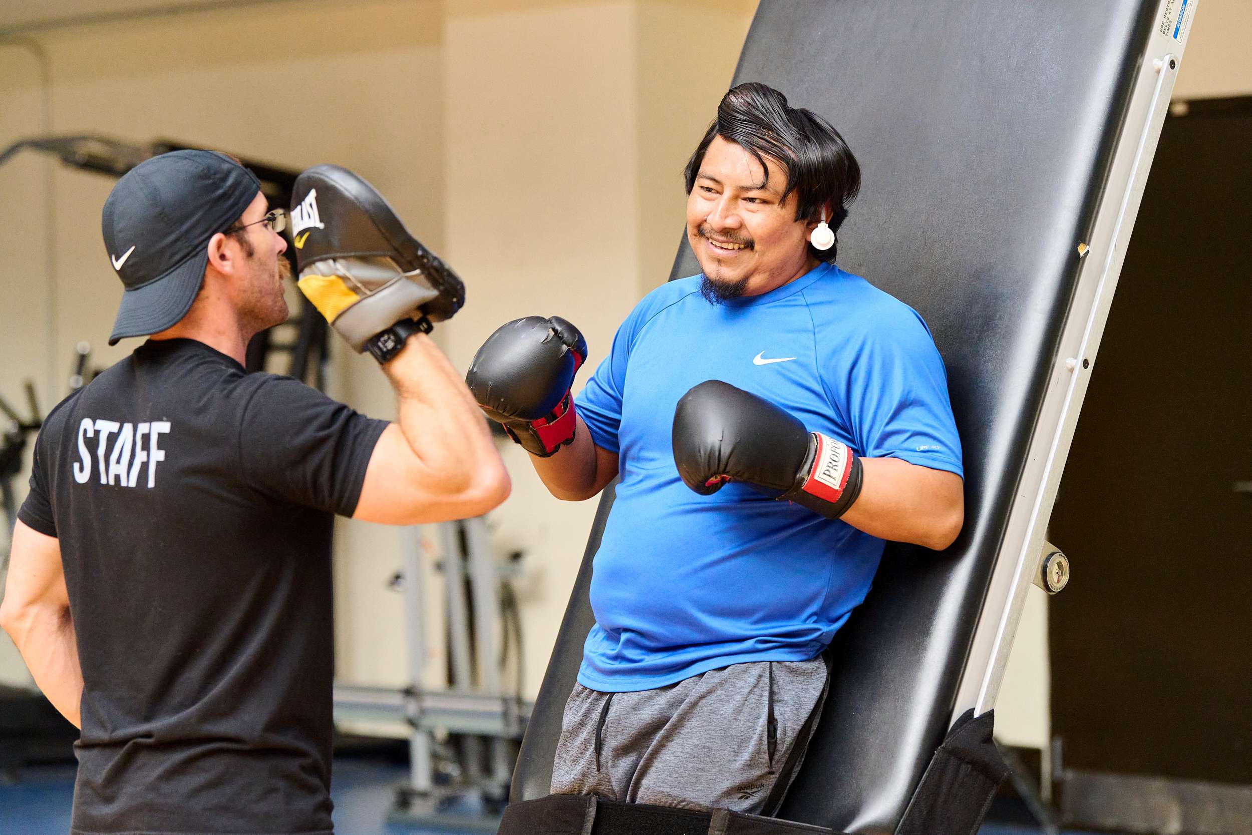 A person with boxing gloves and a happy expression leans against an angled surface, while another person in a 