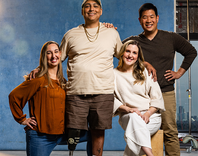 Four adults smiling and posing together in front of a blue background. One man stands in the center with a prosthetic leg, flanked by two women and another man. Everyone appears cheerful and relaxed.