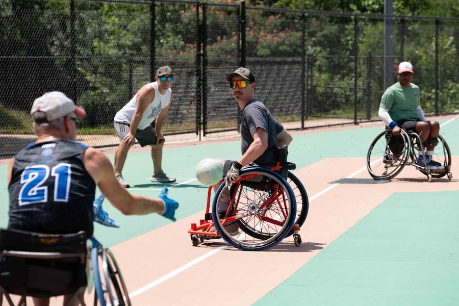 Four men play adaptive wheelchair sports on an outdoor court.