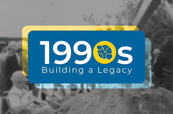 A graphic with the text "1990s Building a Legacy" in white on a blue background. Behind the text, there are faint images of construction workers and equipment. A yellow circle contains three black recycling arrows.